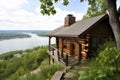 a log cabin perched on a bluff, with a view of the lake below