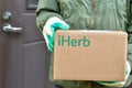 Logo iHerb on cardboard box in courier hands. iHerb is an herbal products company