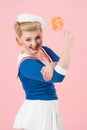 Lollipop can do best concept. Orange big lollipop in hand of attractive blonde female with curls and sailor uniform.