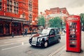 London. Black taxi and Red Telephone Booth on the street with red brick buildings.