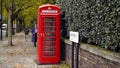 London, Britain-September, 2019: Red telephone booth on street with trees and people. Action. Red public telephone booth Royalty Free Stock Photo