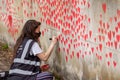 LONDON, ENGLAND- 31 March 2021: Volunteer adding love hearts to The National Covid Memorial Wall near St Thomas` Hospital