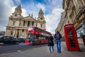 London, England - Tourist couple walking by a traditional red telephone box with red double-decker bus