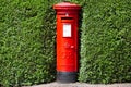 London, England / UK - July 13th 2019: Royal Mail red pillar postbox hidden in green hedge bush