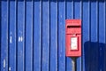 Red Royal Mail post box against blue background wall still in Royalty Free Stock Photo
