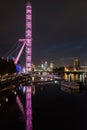 London eye at night being lit by purple lights. Parliament house can be seen in the distance