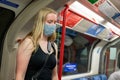 Blonde female wearing PPE face mask traveling on London Underground Tube Train