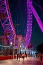 Lower half of The London Eye with people passing by at night