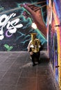 A street musician plays a tuba with fire in the Borough Market in front of a wall with graffiti. London, United Kingdom. Royalty Free Stock Photo