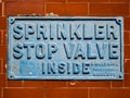 A British `sprinkler stop valve inside` metal wall plate sign.