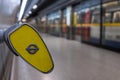 In foreground, end of handrail at Southwark underground station, London showing TFL roundel. In background blurred train arrives a