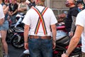 Gay biker with LGBT rainbow braces / suspenders holding up his jeans, talking with other bikers during Gay Pride Parade, London