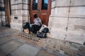 Homeless lady sitting on the pavement, reading book wearing a mask