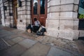 Homeless lady sitting on the pavement, reading book wearing a mask