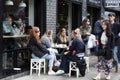 Four blonde girls are sitting at a table in a street cafe, drinking coffee and tea. Late breakfast. There are a lot of people in