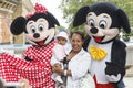 A middle-aged woman with a small child in her arms is photographed with two actors dressed as Mickey Mouse