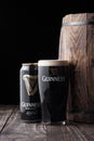 LONDON, UK - MAY 03, 2018: Aluminium can and original glass of Guinness draught stout beer next to wooden barrel on dark wooden ba Royalty Free Stock Photo