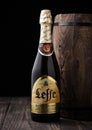 LONDON, UK - MAY 03, 2018: Cold bottle of Leffe beer next to wooden barrel on black background.Leffe is made by Abbaye de Leffe in Royalty Free Stock Photo