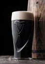 LONDON, UK - MAY 03, 2018: Original glass of Guinness draught stout beer next to wooden barrel on dark wooden background. Royalty Free Stock Photo