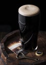 LONDON, UK - MAY 03, 2018: Original glass of Guinness draught stout beer on top of wooden barrel with bottle opener. Royalty Free Stock Photo