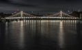 Nocturnal view of floodlit Albert Bridge from Chelsea Bridge with the reflection of the light in very calm water of River Thames