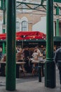 View through the columns of people at a cheese stand inside Borough Market, London, UK.