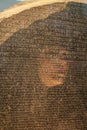 Reflection of womans face in Rosetta Stone as she studies it
