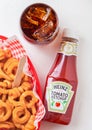 LONDON, UK - SEPTEMBER 10, 2018: Bottle of Heinz tomato ketchup on white kitchen background with glass of cola and curly fries.