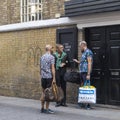 Three fashionably dressed men in short shorts and Hawaiian shirts talk at the brick wall of Bricklane