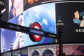 London Underground Tube sign in foreground and large video advertising display in background. Royalty Free Stock Photo