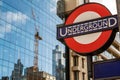 London Underground Tube Station sign with a construction crane and city buildings reflected in a modern glass office building in Royalty Free Stock Photo