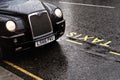 London, United Kingdom - February 01, 2019: Iconic black cab driving on the road near yellow taxi sign on wet asphalt road,