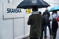 London, United Kingdom - February 01, 2019: Pedestrians with umbrellas walking near wooden barrier at construction site with label Royalty Free Stock Photo