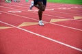 Lone runner legs and feet race down a red numbered athletic track