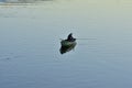 A lone angler on a boat in the middle of the river on a quiet day. Summer