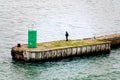 Lone angler standing on a pier by the ocean