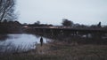 A lone atmospheric figure, standing by a lake edge, looking out up at a motorway bridge with traffic trails, winters evening Royalty Free Stock Photo