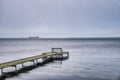 Lone bench on a thin boardwalk at sea and a faraway vessel amid winter gloominess covey sadness, solitude and desolation feelings Royalty Free Stock Photo