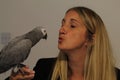 A lone Caucasian woman kissing her pet African Grey Parrot that is perched in her hand Royalty Free Stock Photo