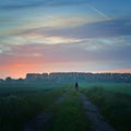 A lone figure on a country path looking at the first misty light of sunrise