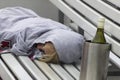 A person sleeping on a bench with a bottle of wine