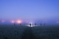 A lone figure with a torch standing in a field as ghostly blurred figures appear on a spooky, misty night
