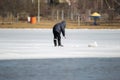 A lone fisherman is bent over a hole in the ice and is trying to catch a fish Royalty Free Stock Photo