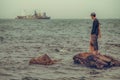 Lone fisherman gazes out at large fishing boat.