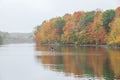 Lone fisherman in a kayak fishes near trees in beautiful autumn color on a calm overcast day