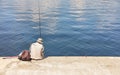 A lone fisherman sits on a concrete pier with a fishing rod near the water on a summer sunny day Royalty Free Stock Photo