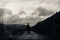 A lone hiker looking up a hill on a mysterious, moody mountain road. With a dark, grunge, vintage edit