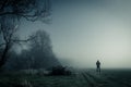 A lone hooded figure standing on a path on a spooky misty night, with a cold blue edit