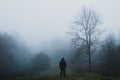 A lone hooded figure standing on a woodland path on a cold, foggy winters day. With a blue muted edit Royalty Free Stock Photo