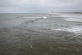 A lone male surfer wearing a wet suit is seen alone in a rough ocean on an overcast day